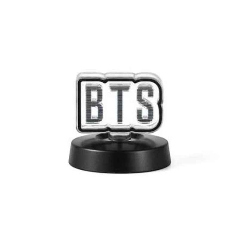 A small BTS-themed decorative item featuring the letters 'BTS' in a black-and-white striped pattern inside a silver-bordered rounded rectangle, mounted on a round black base against a light gray background.