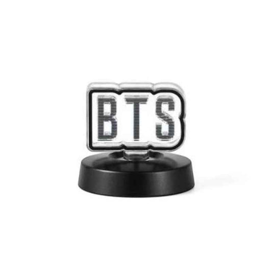 A small BTS-themed decorative item featuring the letters 'BTS' in a black-and-white striped pattern inside a silver-bordered rounded rectangle, mounted on a round black base against a light gray background.