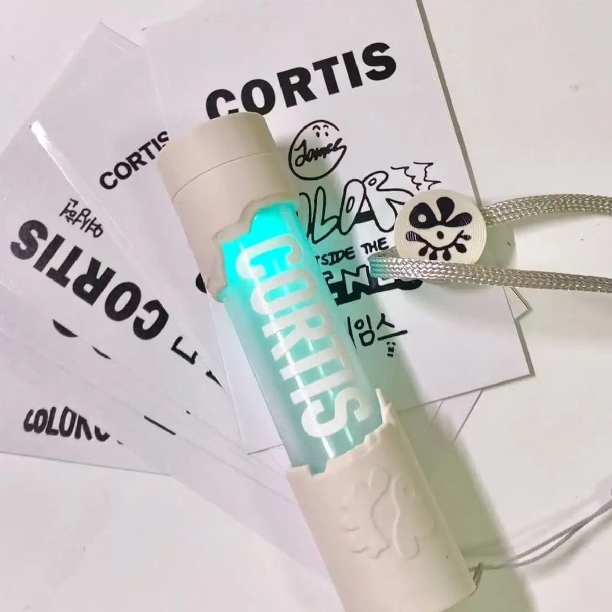 CORTIS mini LED lightstick keychain glowing cyan with a white textured casing